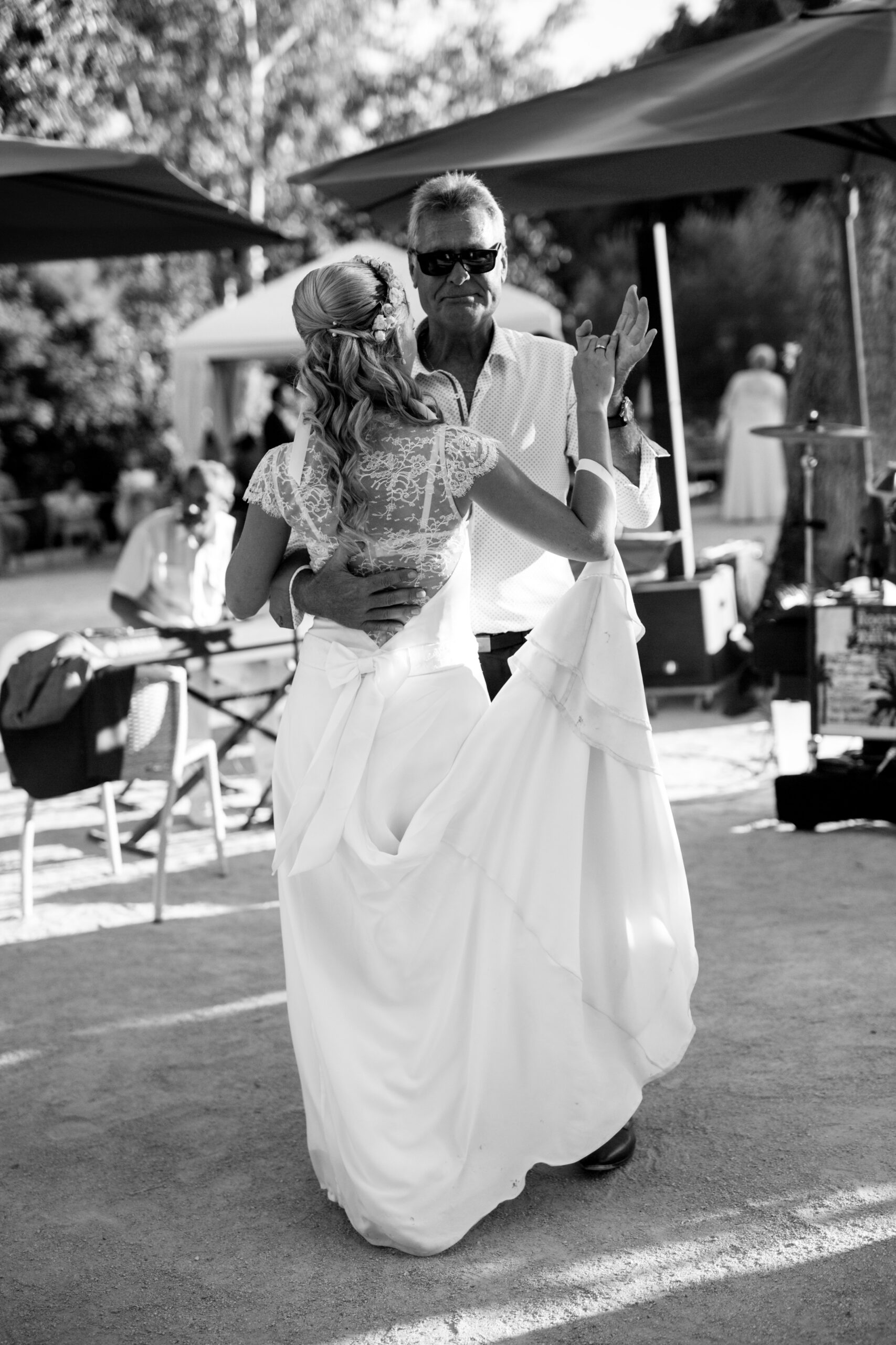 Mariée vue de dos en train de danser avec son oncle portant une robe de mariée en soie et dentelle. Jolie instant de complicité familiale.